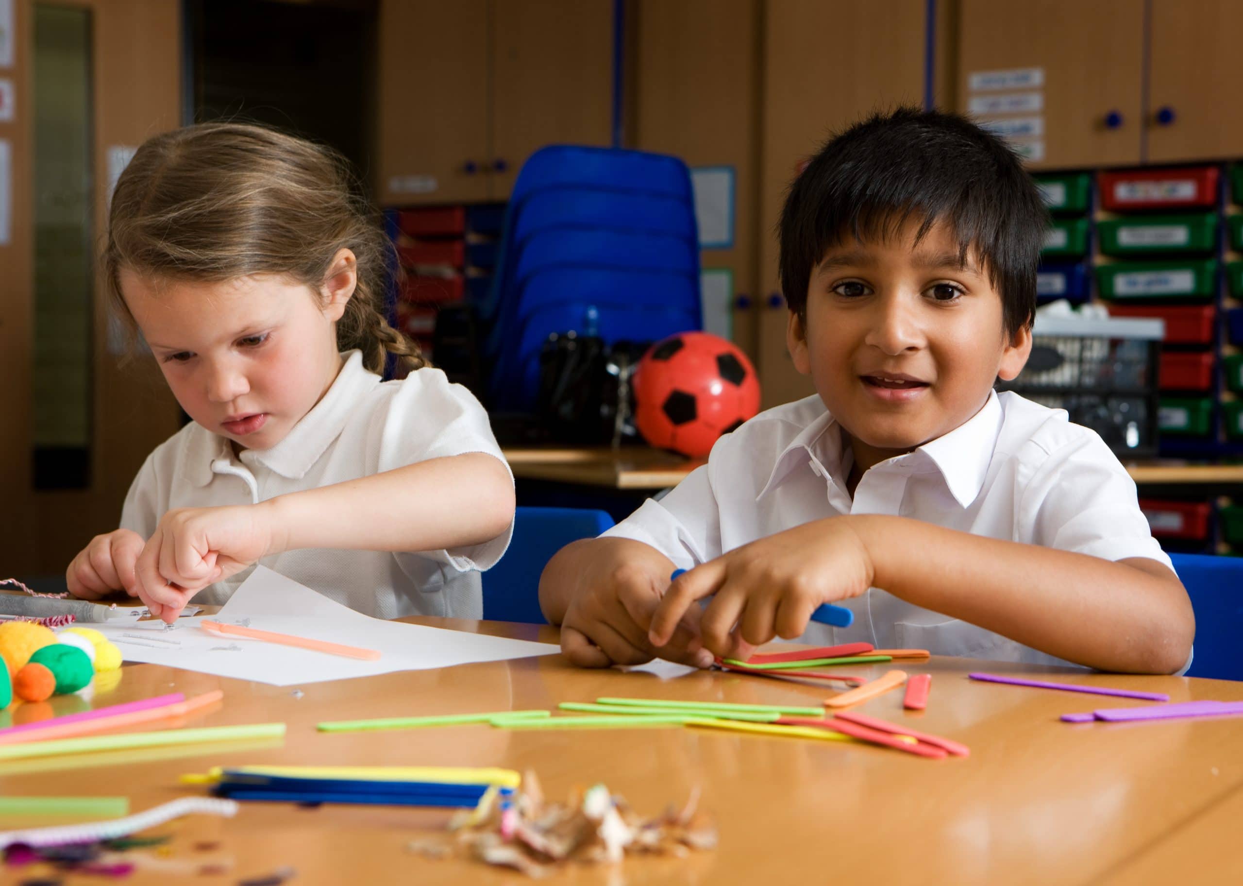 Elementary School: Creative Play. A happy glance from a primary school boy of South Asian heritage at play with a fellow pupil in their classroom.